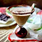 Square image of the chocolate peppermint martini with a dark background, chocolate shavings on top, and peppermint sticks as a garnish