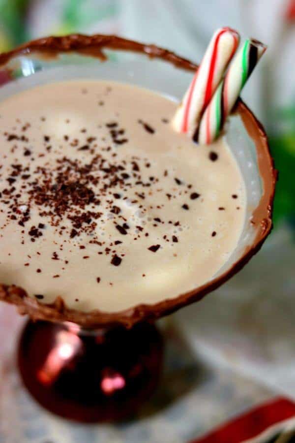 Looking down at the surface of a chocolate peppermint martini with grated chocolate floating on the top and a red and green peppermint stick garnish.