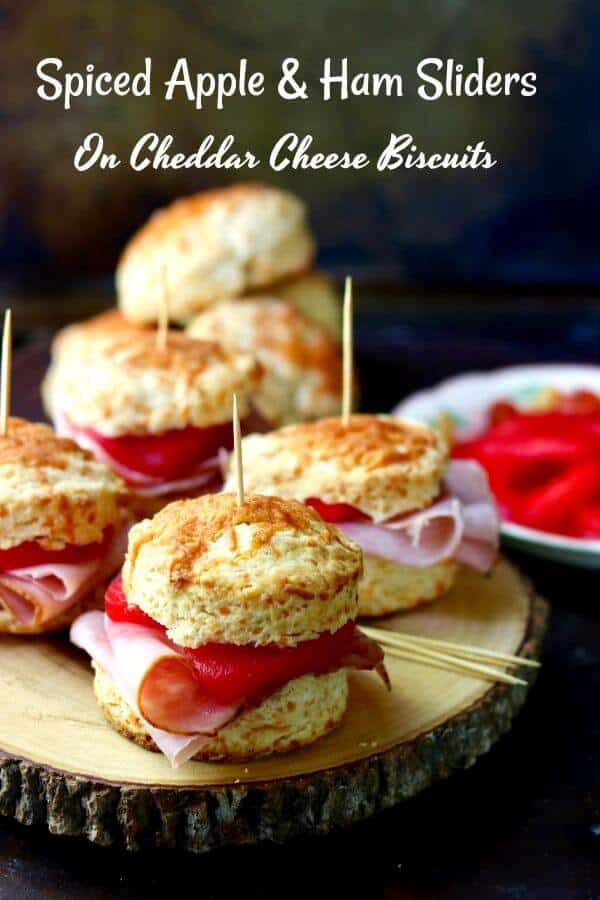 Wooden tray with spiced apple and ham sliders made with cheddar cheese biscuits.