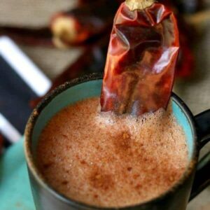 Spiked mexican hot chocolate drink in a black and tea mug with a chile as garnish