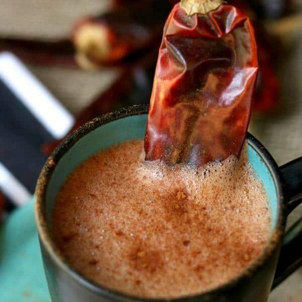 Spiked mexican hot chocolate drink in a black and tea mug with a chile as garnish