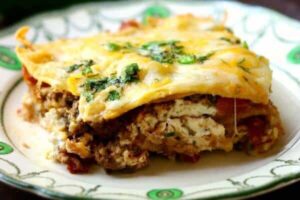 mexicanlasagna layersoftortillas,cheese,andtacomeatservedonavintageplate.Usedasanillustrationonpageaboutauthormaryeaudet