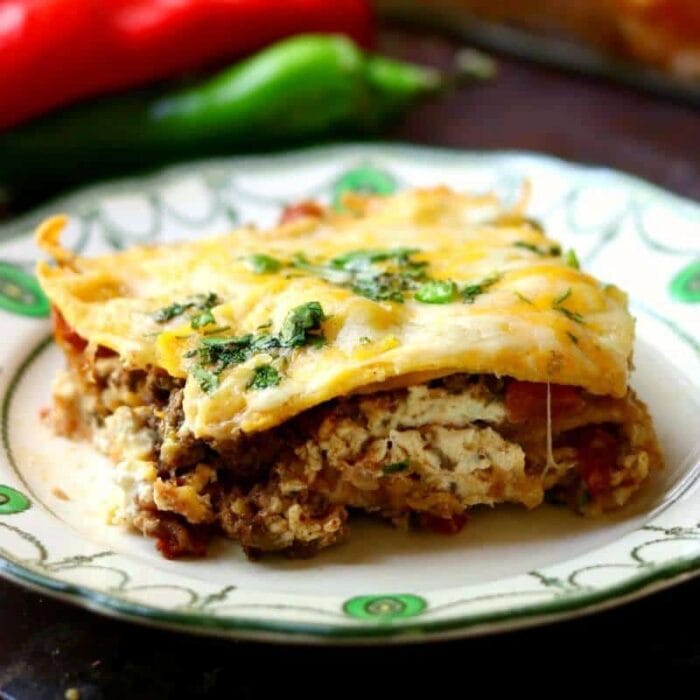 Spicy meat and gooey cheese ooze out of a cut piece of the easy mexican lasagna recipe topped with cilantro.