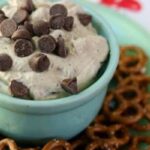 peanut butter chocolate chip cheesecake dip in a jadite bowl surrounded with crunchy pretzels