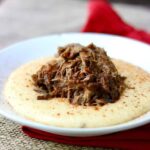 Tender slow cooker pot roast on a bed or jalapeno cheese grits in a white bowl.