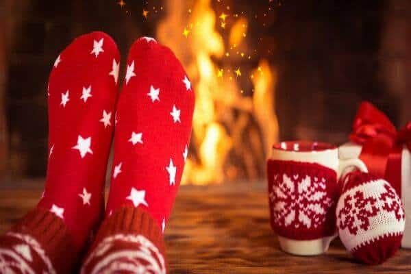 a person's feet in red socks with white stars in front of a fireplace. A cup of coffee is to the side. Feature image for best gifts for coffee lovers