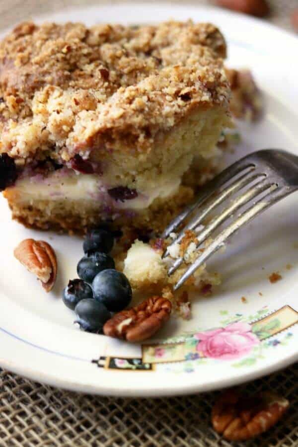 A piece of blueberry cream cheese coffee cake on a white plate with a silver folk upside down on the plate - closeup