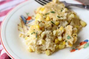 A closeup image of southern corn pudding on a white plate with a fork in the background. Feature image for this article.