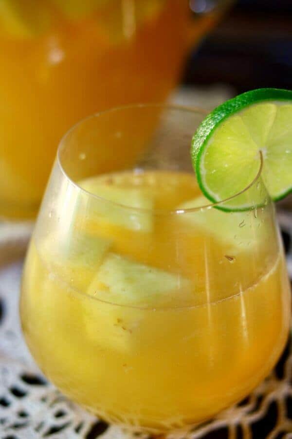 Closeup of a glass filled with tropical pineapple sangria garnished with a lime. Pineapple floats in the yellow sangria.