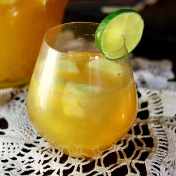 Square image of a glass of tropical pineapple sangria on a lace cloth.