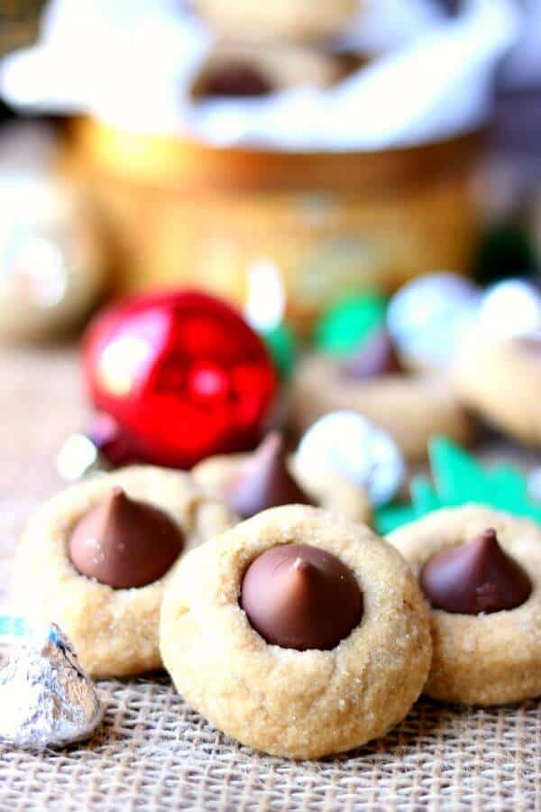 A peanut butter blossoms recipe straight from your childhood, this Hershey's classic is soft and chewy just like you remember. This easy peanut butter cookie recipe goes together fast, freezes well, and is full of chocolate and peanut butter flavor. Includes variations and tips for freezing peanut butter kiss cookies. #cookiesrecipe #easychristmascookies #bestpeanutbuttercookies close up of peanut butter kiss cookies with christmas ornaments in the background. Peanut butter blossoms recipe image2