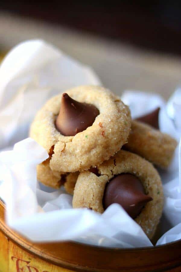 A peanut butter blossoms recipe straight from your childhood, this Hershey's classic is soft and chewy just like you remember. This easy peanut butter cookie recipe goes together fast, freezes well, and is full of chocolate and peanut butter flavor. Includes variations and tips for freezing peanut butter kiss cookies. #cookiesrecipe #easychristmascookies #bestpeanutbuttercookies Peanut butter blossoms cookie in a metal container with white tissue paper - peanut butter blossoms recipe image 3