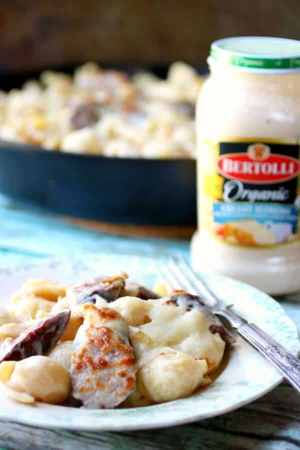 closeup of sausage alfredo with a jar of Bertolli Organic Alfredo sauce in the background.