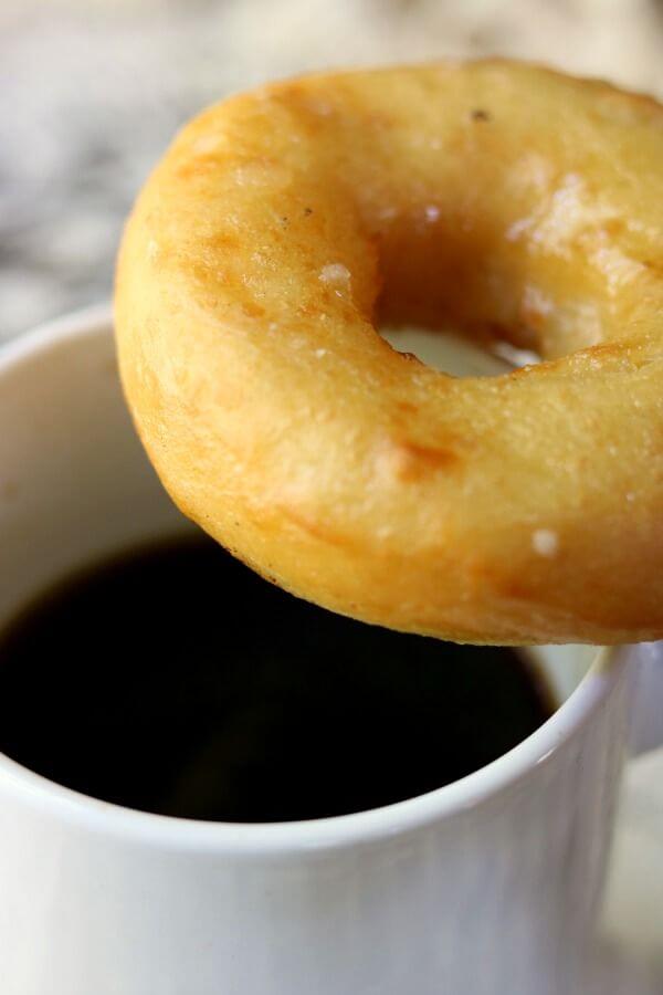 Closeup of a glazed donut balanced on a white coffee cup - donuts made from this homemade donut recipe