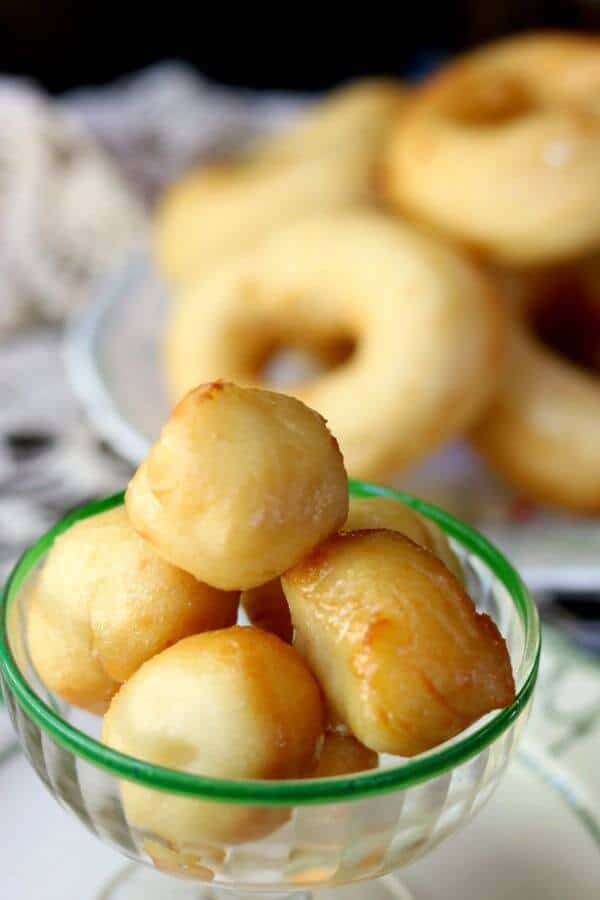 Homemade glazed donut holes in a vintage sherbet glass with homemade yeast donuts in the background- homemade donut recipe image 2