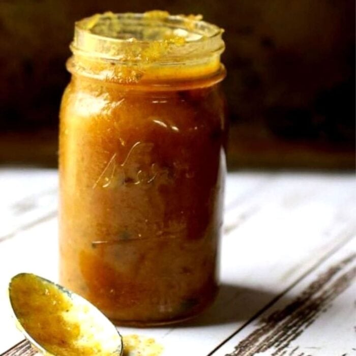 a jar of yellow jezebel sauce on a white wooden table.