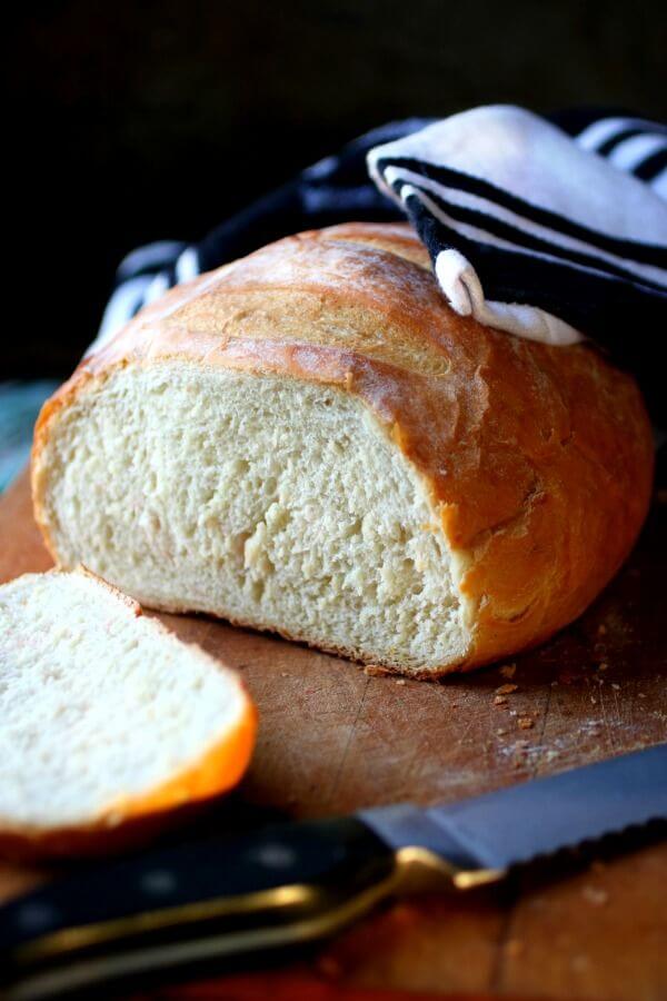 A baked loaf of rustic bread is baked and sliced on the table.