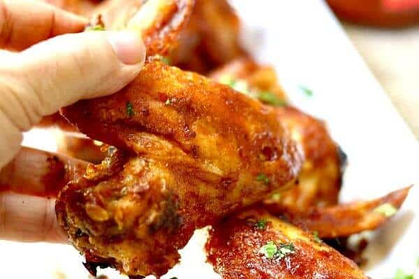Spicy oven baked chicken wings are being picked up with fingers.