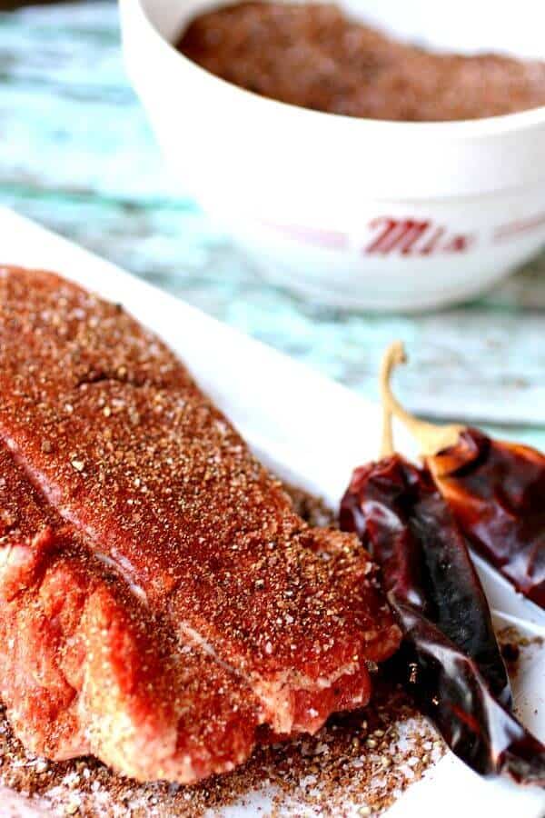 Large piece of steak in the foreground covered with homemade dry rub mixture to show texture.