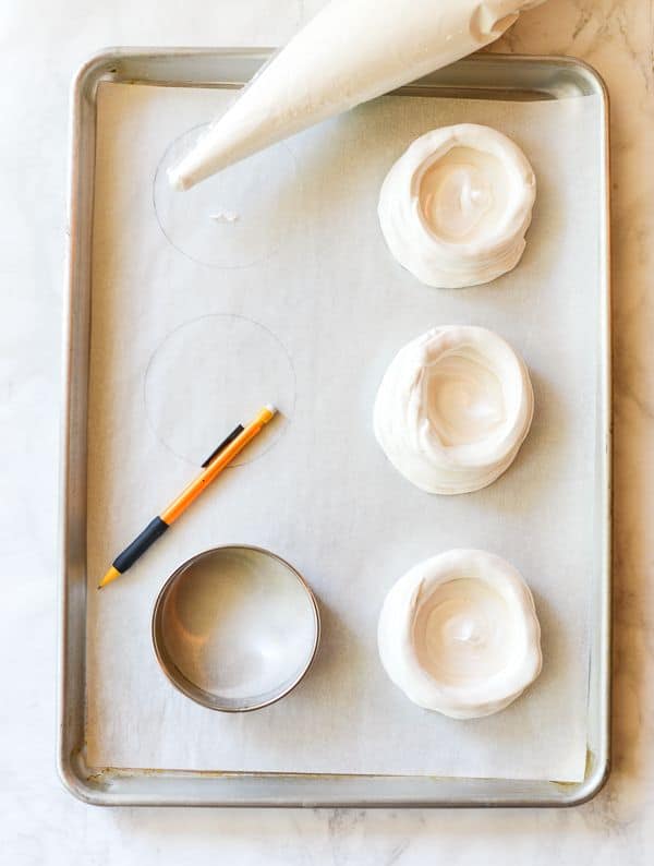 Three unbaked meringue shells for the Pavlova recipe are on a cookie sheet.