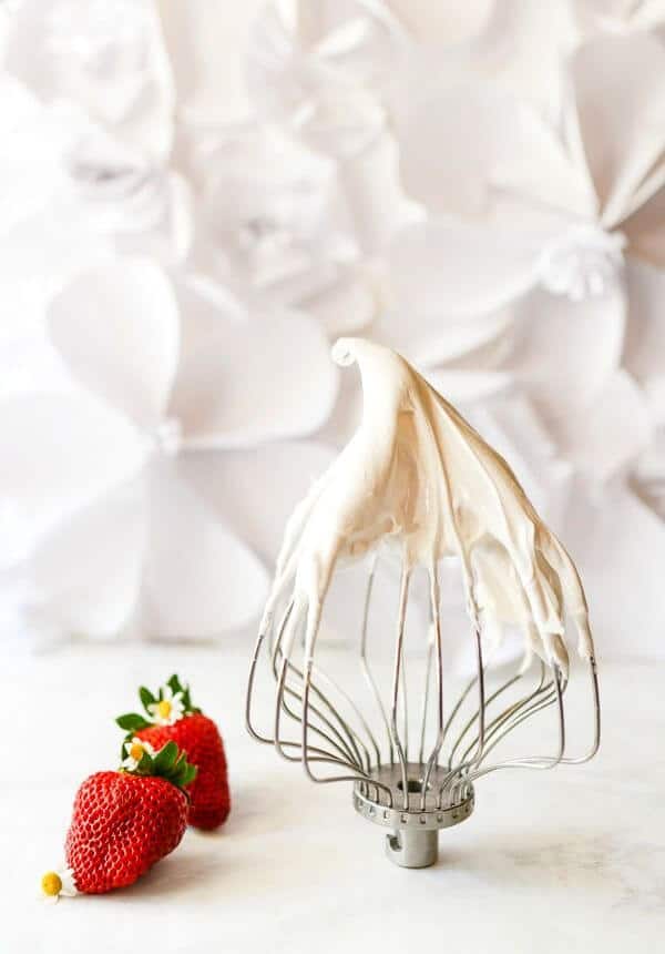 Two strawberries are placed near a balloon whisk covered in white meringue for the Pavlova recipe