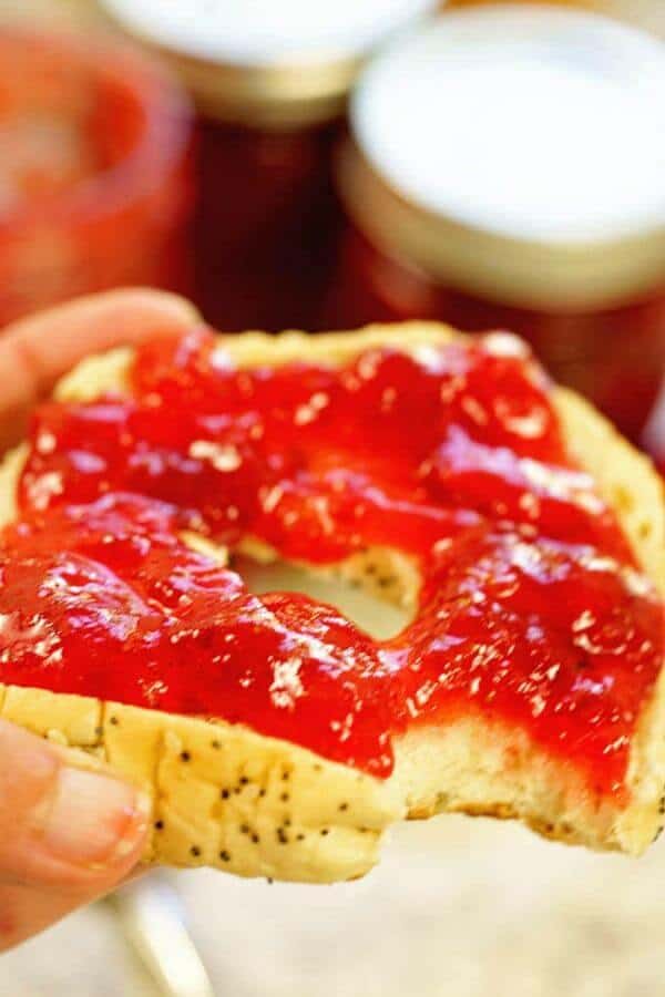 Easy homemade strawberry jam is spread on a bagel with a bite taken out of it