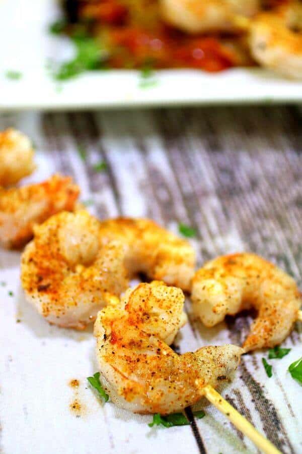 Skewered shrimp creole are on a table next to a platter of creole shrimp