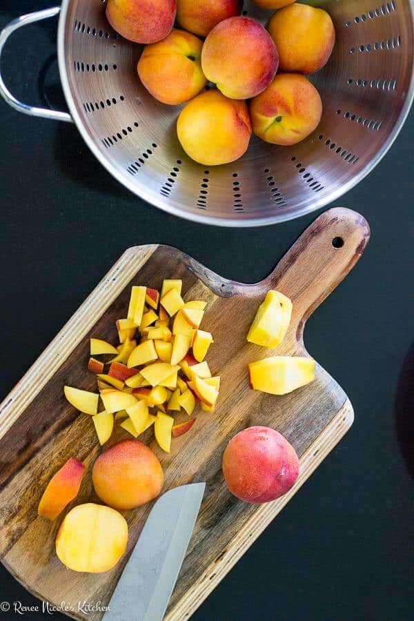 Easy peach cobbler recipe has a splash of bourbon. You'll love this classic southern dessert! #restlesschipotle #dessert #recipe #bourbon #peaches #southern #cobbler #oldfashioned chopped peaches on a cutting board.