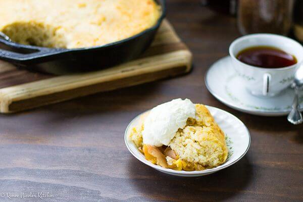 A dish of peach cobbler with whipped cream on top and a coffee cup to the side.