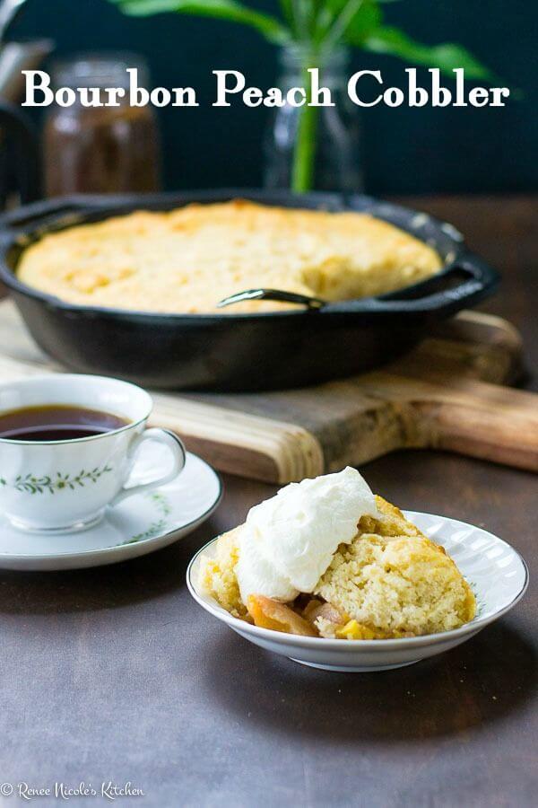 A serving of bourbon peach cobbler with whipped cream on top in a dish. a coffee cup and iron skillet are in the background. Title image