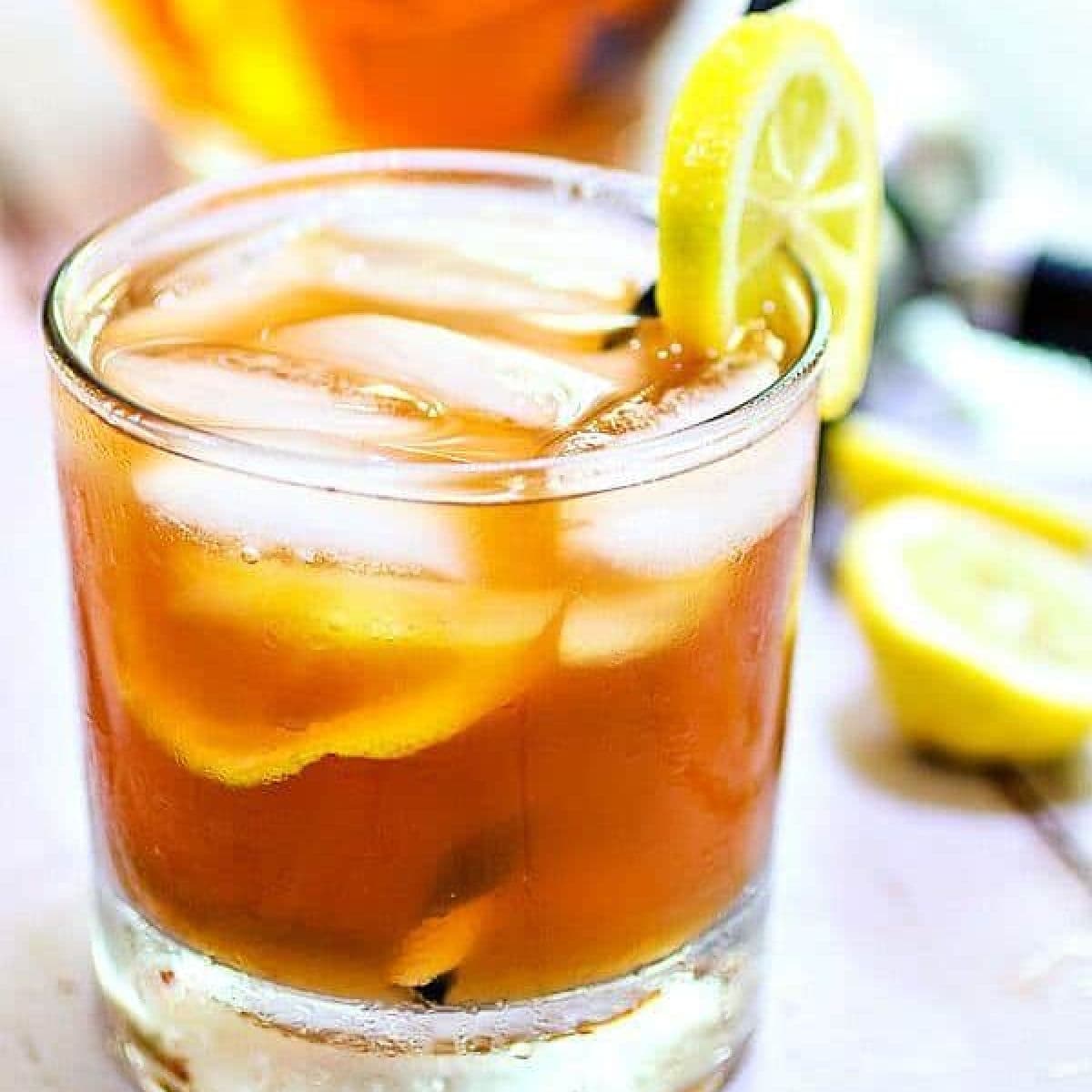 An on the rocks glass with a cocktail and ice in it garnished with lemon.