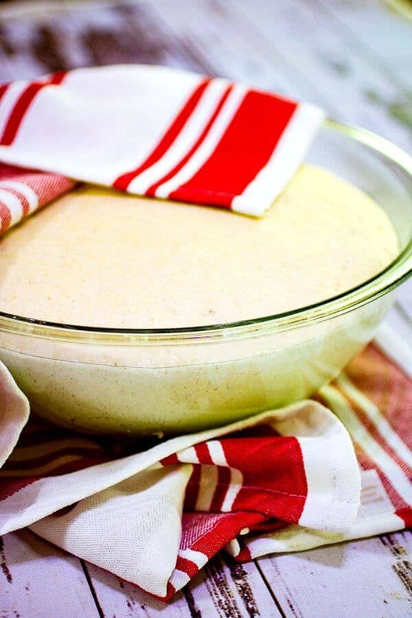 A glass bowl with pizza dough rising in it.