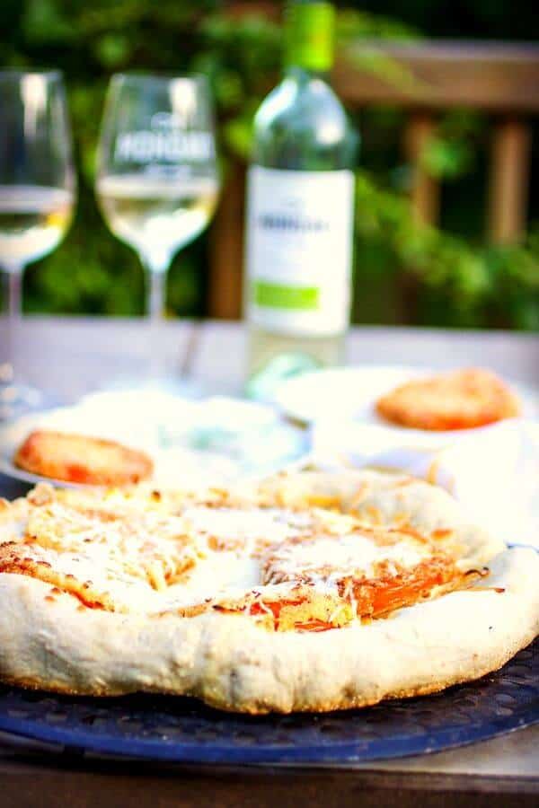 A whole pizza with wine in the background.
