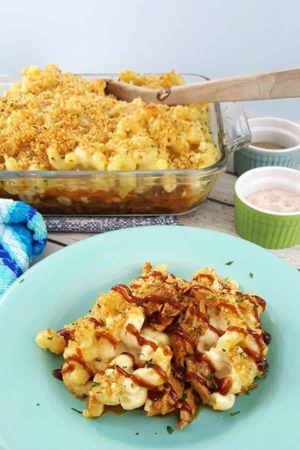 Mac and cheese with pulled pork on an aqua plate with a casserole dish in the background