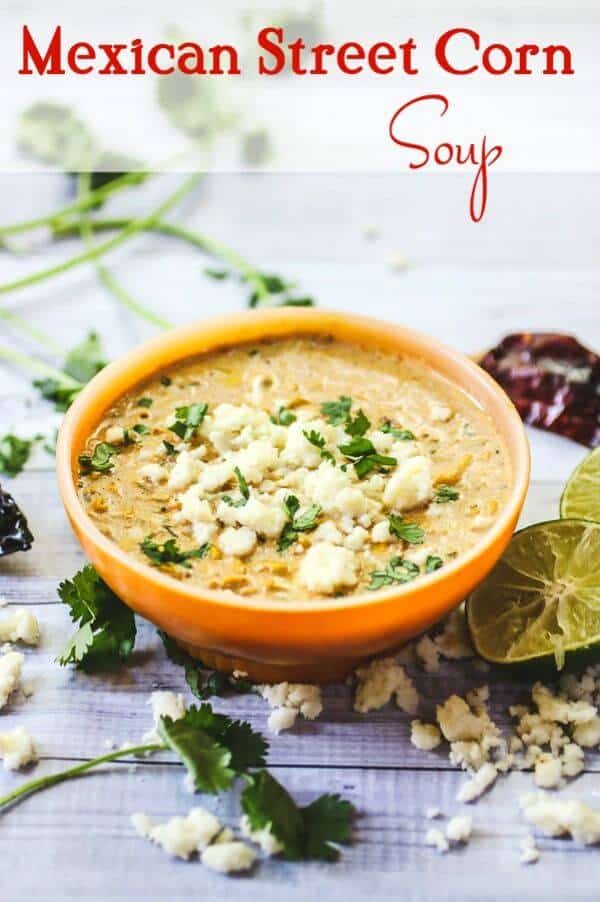 A bowl of corn soup surrounded by herbs.