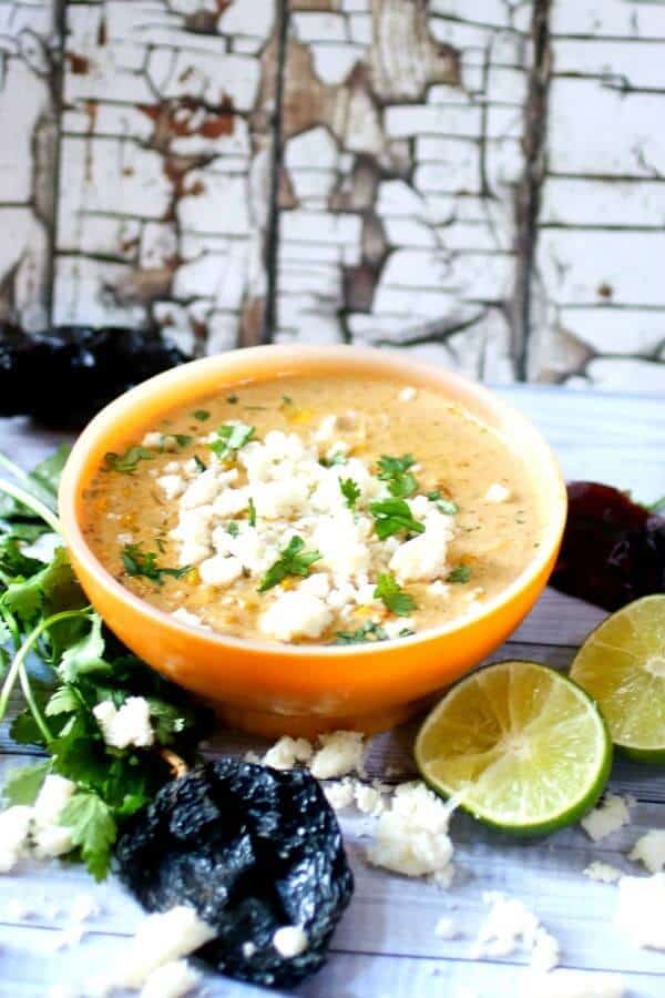 An orange bowl of Mexican Street Corn soup with limes at the base