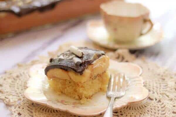 A square of cake on a plate with a teacup in the background