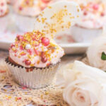 A pink cupcake on a lace doily with a rose.