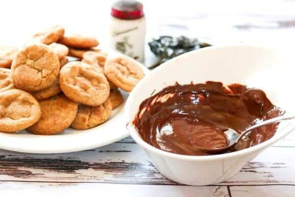 Melted chocolate in a white bowl with cookies in the background.