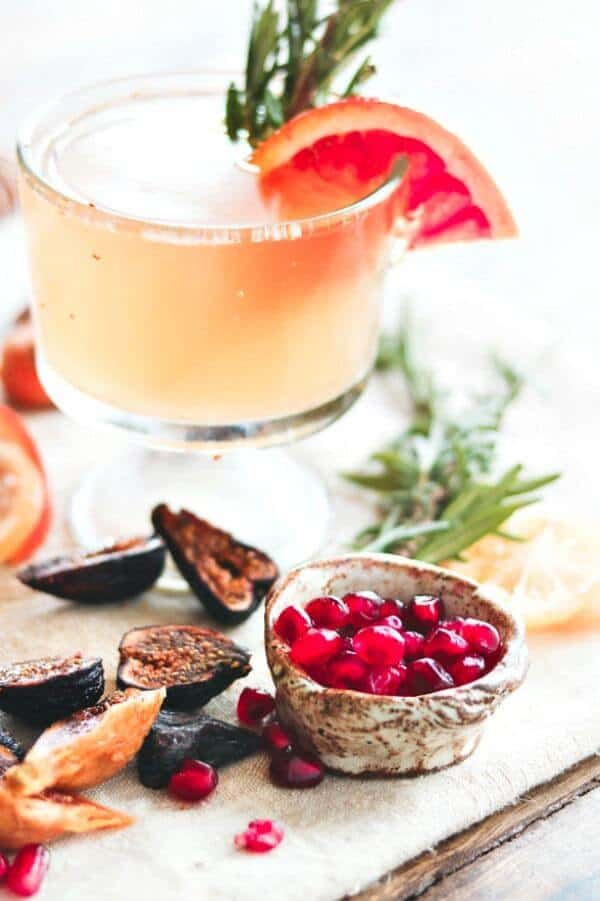 Closeup of old fashioned cocktail in a stemmed glass with pomegranate seeds in a bowl.