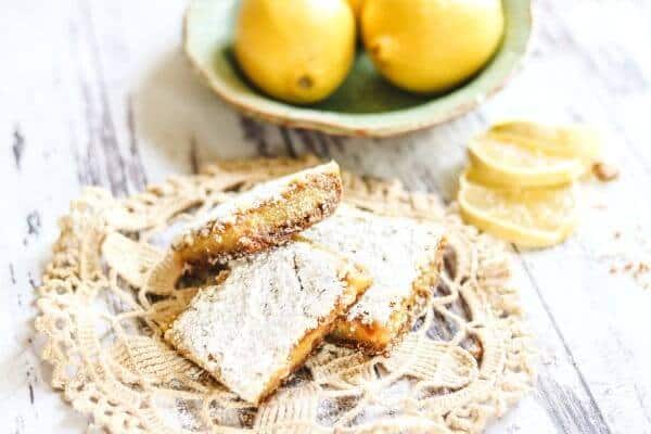 Lemon bars on a table with a bowl of lemons in the background.
