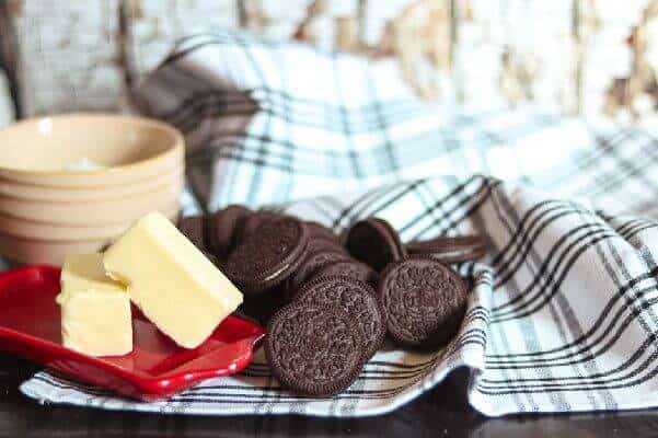 A stick of butter, Oreo cookies, and a bowl on a black and white towel.