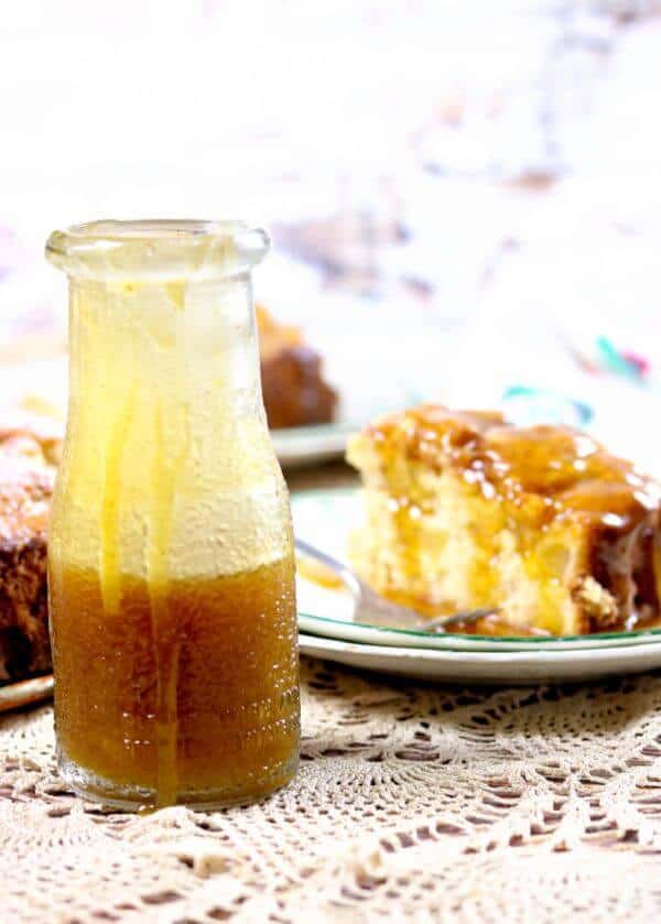 A small bottle of whiskey butter sauce with a slice of cake in the background.