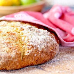 Round loaf of crusty Irish soda bread partway covered with a red towel