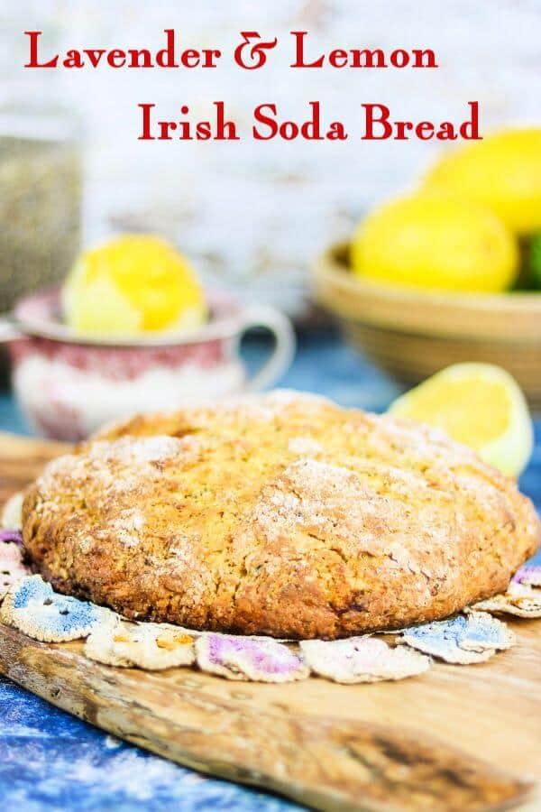 A round loaf of Lavender Lemon Irish Soda Bread on a wooden board. Lemons in the background