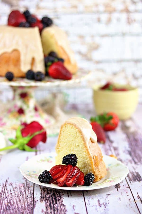 A slice of cake garnished with berries in the foreground  with the cake plate in the background