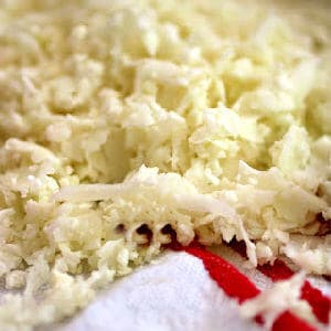 A pile of grated cauliflower on a white and red tea towel