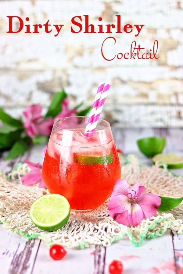 A red cocktail with pink striped straws in it sits on a lace topped table. Text says "Dirty Shirley Cocktail"