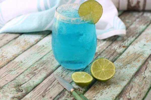 A glass filled with light blue lemonade and garnished with limes.