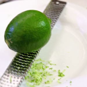 A lime on a microplane being grated into a bowl.